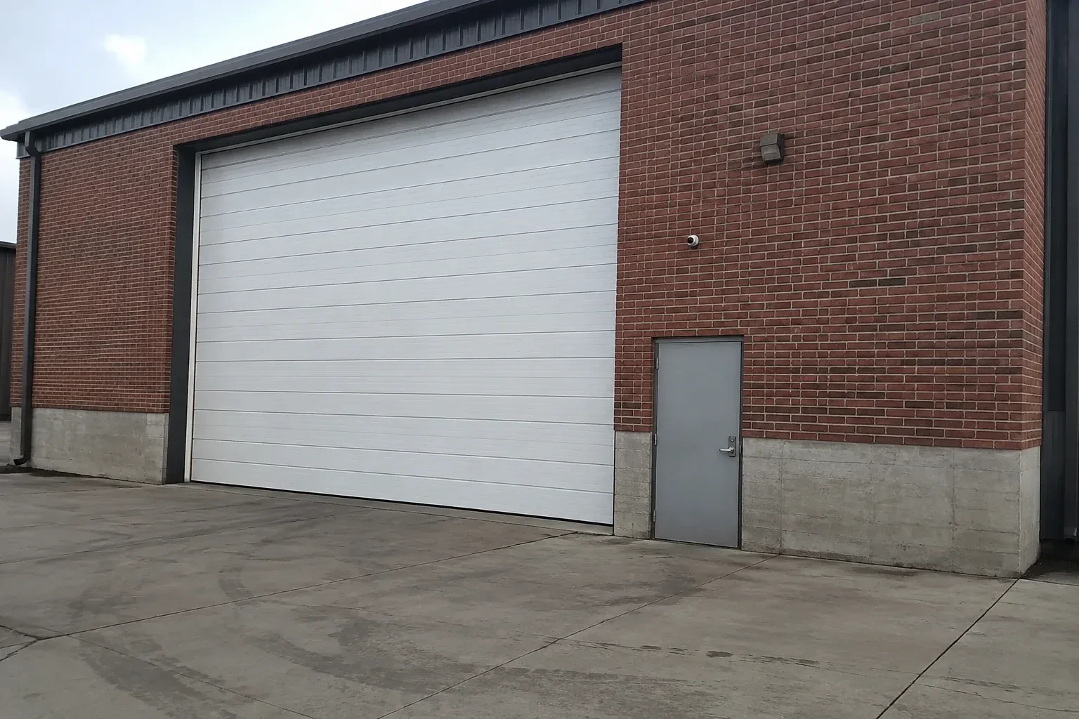 Tall closed sectional loading door beside a personnel door at a brick unit. — Commercial Sectional Door Repair, Haldimand County
