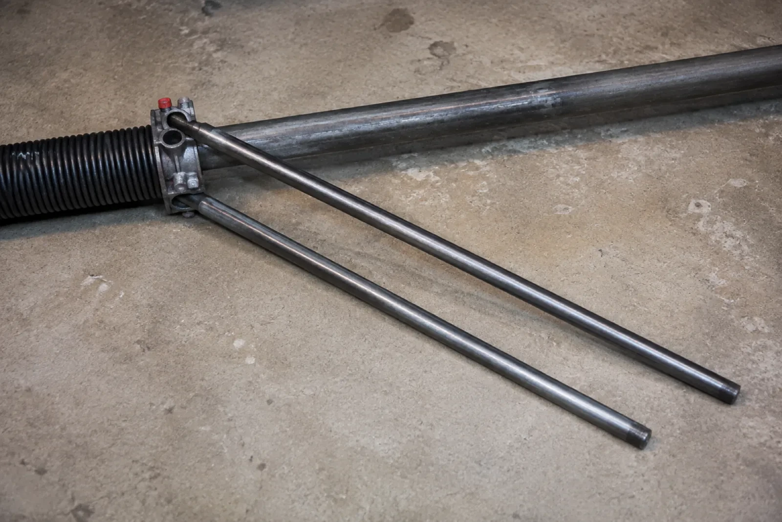 Two long steel winding bars inserted into the cone of a black torsion spring lying on a concrete floor. — Nanticoke